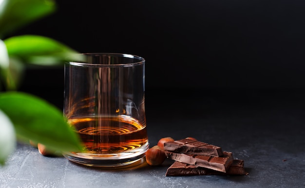 Conhaque ou uísque ou conhaque em um copo. pedaços de chocolate e avelãs.