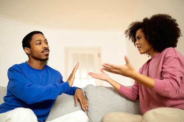 Cônjuges afro-americanos brigando sentados no sofá em casa