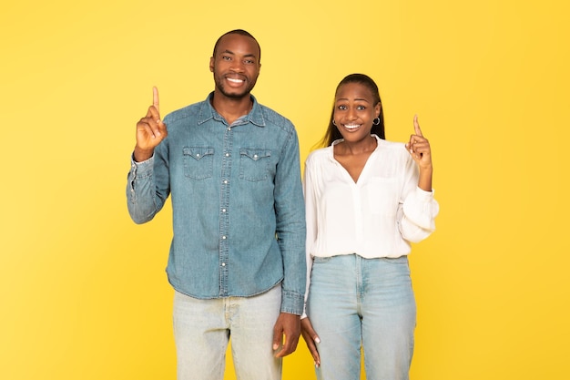 Cônjuges afro-americanos felizes apontando os dedos para cima sobre fundo amarelo