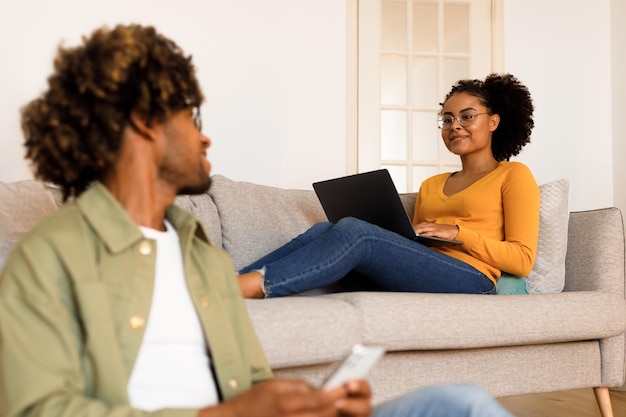 Cônjuges afro-americanos navegando na web via smartphone e laptop dentro de casa