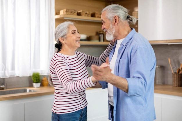 Cônjuges felizes amando marido e esposa sênior dançando no interior da cozinha