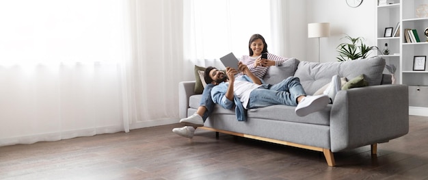 Foto cônjuges indianos relaxados descansando no sofá em casa usando gadgets