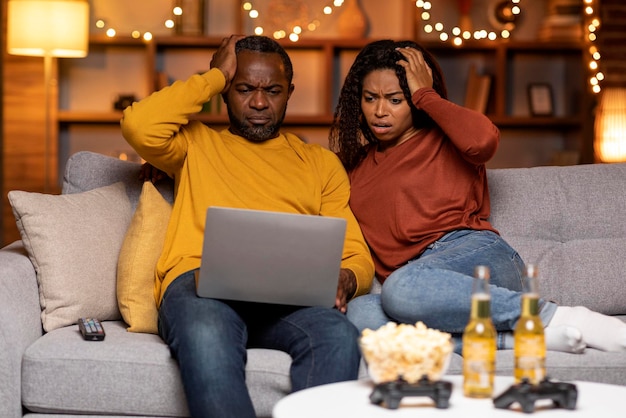 Cônjuges negros chocados olhando para o interior da casa da tela do laptop