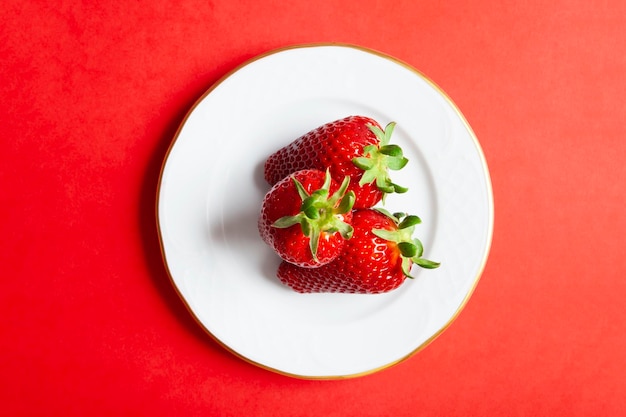 Foto conjunto de 3 fresas en un plato sobre fondo rojo.