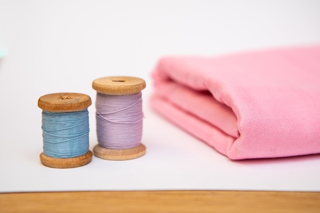 Conjunto de accesorios de confección. Cerca de una pila de tela rosa doblada, tijeras de coser y carretes de hilo