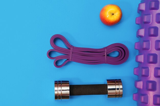 Conjunto de accesorios deportivos rodillo de masaje, arnés deportivo, auriculares sobre un fondo azul.