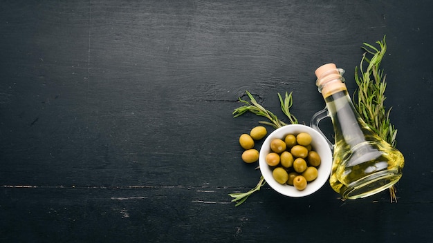 Un conjunto de aceitunas y aceite de oliva y romero Aceitunas verdes y aceitunas negras Sobre un fondo de madera negra Espacio libre para texto