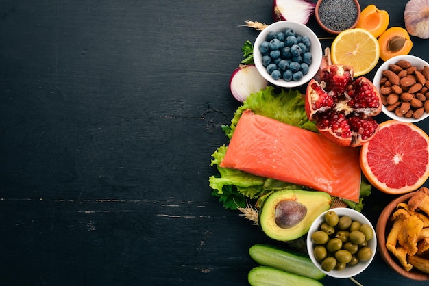 Un conjunto de alimentos saludables Pescado nueces proteínas bayas verduras y frutas Sobre un fondo de madera negra Vista superior Espacio libre para texto