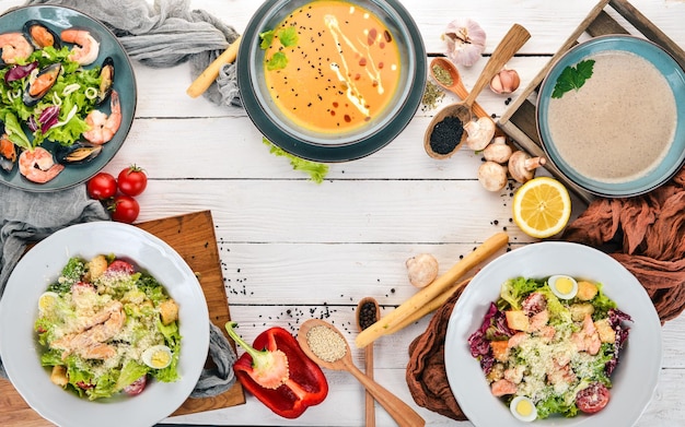 Un conjunto de alimentos saludables en platos Ensalada César Mariscos Sopa de calabaza y champiñones Vista superior Sobre un fondo de madera Espacio de copia