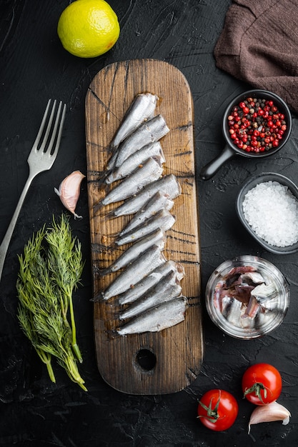 Conjunto de anchoas enlatadas, sobre tabla de cortar de madera, en negro