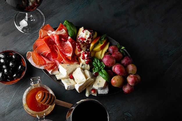 Un conjunto de aperitivos para vino, jamón, pepperoni, queso, uvas, melocotón y aceitunas en una vista superior de la placa.