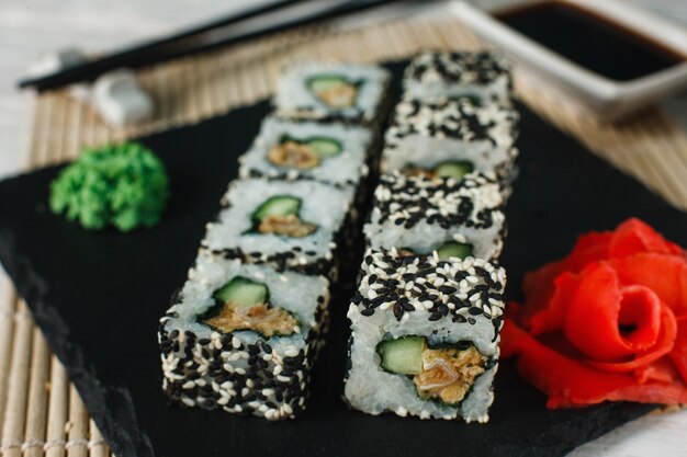 Conjunto apetitoso e fresco de uramaki com gergelim servido em ardósia preta, closeup. Comida japonesa saudável, sushi, frutos do mar.