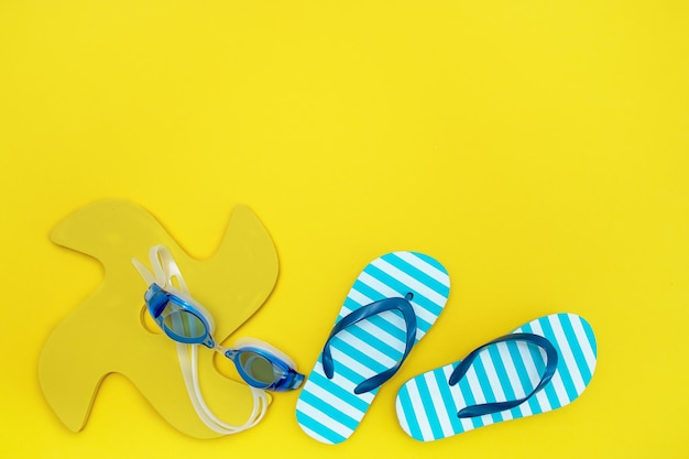 Conjunto de artículos para el juguete de playa, gafas de natación, chanclas para niños sobre fondo amarillo