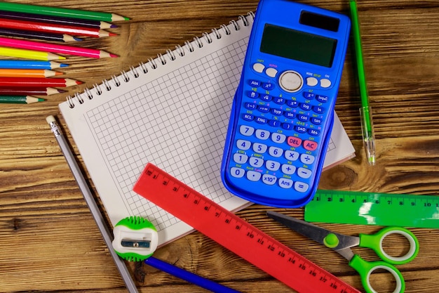 Conjunto de artículos de papelería escolar Bloc de notas en blanco calculadora reglas lápices bolígrafos tijeras y sacapuntas en el escritorio de madera Vista superior