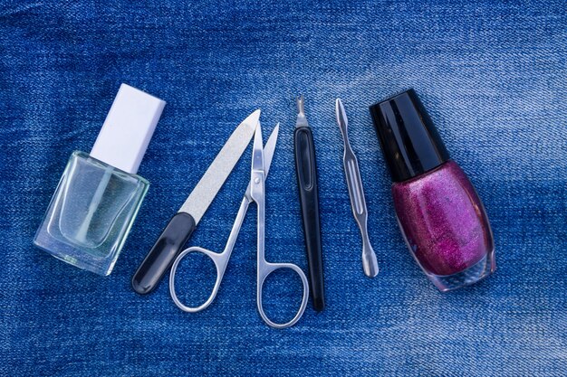 Conjunto básico de herramientas de manicura sobre fondo de jeans. Tijeras para uñas y cutículas, recortador de cutículas, lima de uñas, esmalte de uñas