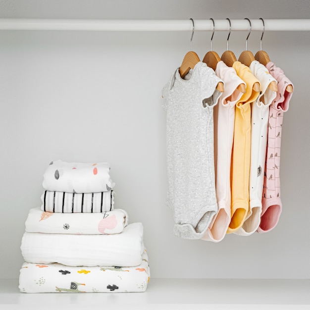 Conjunto de body de bebé para niña y niño recién nacido en perchas en  armario blanco. la maternidad, la limpieza del armario de los niños en  casa. concepto de moda mínima.