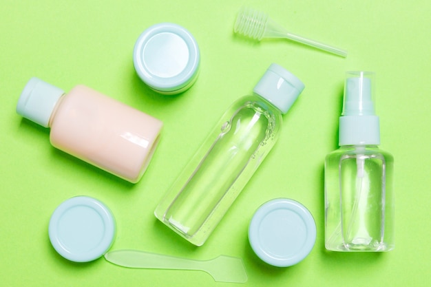 Conjunto de botellas de cosméticos de tamaño de viaje sobre fondo verde. Endecha plana de tarros de crema. Vista superior del concepto de estilo de cuidado corporal.