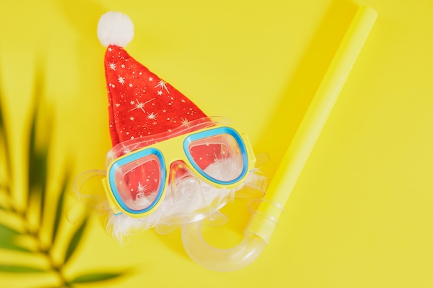 Conjunto de buceo, sombrero de santa claus y hojas de palmera sobre fondo amarillo, vacaciones de Navidad en la playa