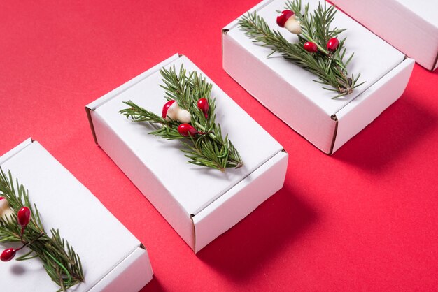 Conjunto de cajas de cartón blancas decoradas con adornos de árbol de Navidad sobre fondo rojo.