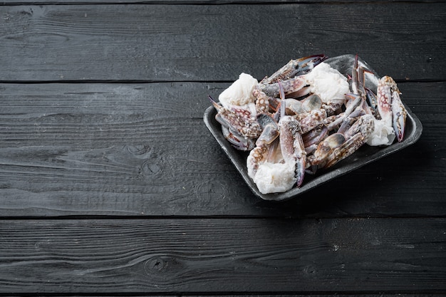 Conjunto de carne de cangrejo azul natación cruda congelada, en bandeja de plástico, sobre mesa de madera negra