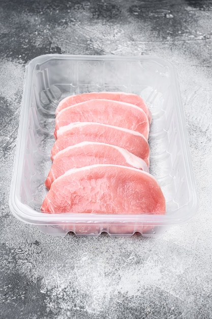 Conjunto de carne de filete de cerdo cruda, en un recipiente de plástico, sobre fondo de mesa de piedra gris