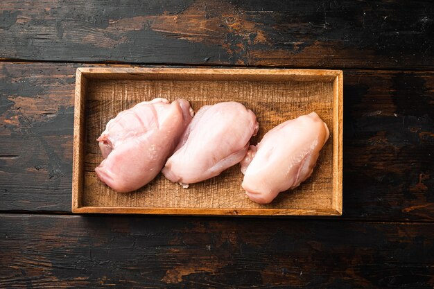 Conjunto de carne de pollo fresca, en caja de madera, sobre la vieja mesa de madera oscura.