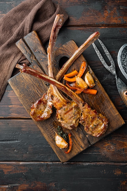 Conjunto de chuletas de cordero asado tradicional, sobre tabla de servir de madera, sobre la vieja mesa de madera oscura, vista superior plana