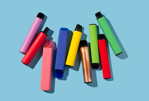 Conjunto de coloridos cigarrillos electrónicos desechables sobre un fondo azul. El concepto de fumar moderno.
