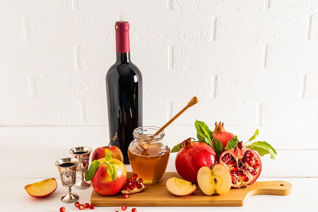 Un conjunto de comida tradicional y una botella de vino tinto para Rosh Hashaná contra el telón de fondo de una pared de ladrillo blanco vista frontal Año Nuevo judío