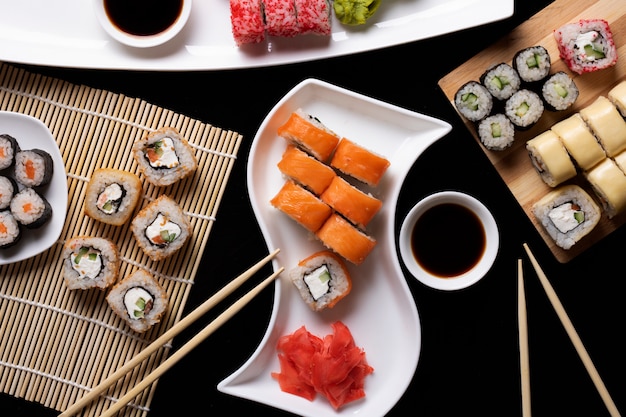 Conjunto de comida tradicional japonesa en una mesa oscura. Rollos de sushi, nigiri, filete de salmón crudo, arroz, queso crema, aguacate, lima, jengibre en escabeche.