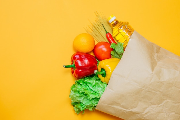 Un conjunto de comida vegetariana, pimienta, chile, aceite de girasol, tomate, naranja, pasta, lechuga en un paquete de papel artesanal, en un espacio naranja