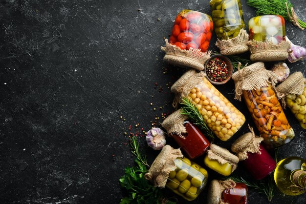 Conjunto de conservas de verduras y champiñones en frascos de vidrio Conjunto de alimentos en escabeche sobre fondo de piedra negra Vista superior