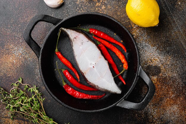 Conjunto de corte de pescado crudo, con ingredientes y hierbas de romero, sobre fondo de mesa rústico oscuro antiguo, vista superior plana