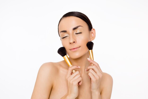 Conjunto cosmético Cosméticos de maquillaje Hermosa mujer sonriente joven con una piel limpia sostiene un cepillo para polvo