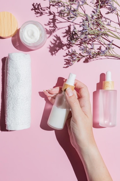 Conjunto de cosméticos para el cuidado de la piel en paquete de clase esmerilado blanco con tapas de bambú sobre fondo rosa Mano femenina sosteniendo una botella con crema