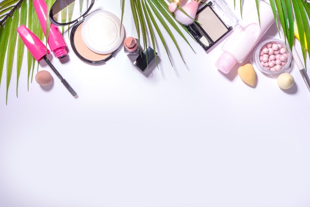 Conjunto de cosméticos decorativos de verano, maquillaje profesional y accesorios sobre fondo blanco con hojas de palma, espacio de copia de vista superior plana