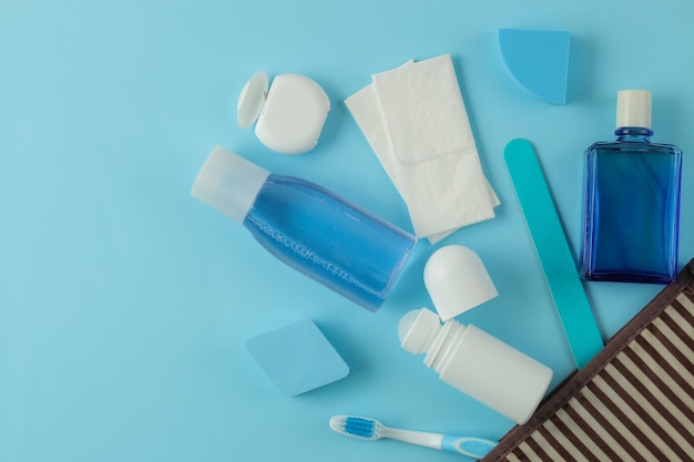 Un conjunto de cosméticos y productos de cuidado personal para viajar en una bolsa de cosméticos sobre un fondo azul claro. vista superior. cosméticos de viaje