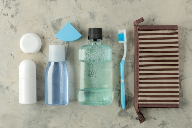 Un conjunto de cosméticos y productos de cuidado personal para viajar en una bolsa de cosméticos sobre un fondo de hormigón claro. vista superior. cosméticos de viaje