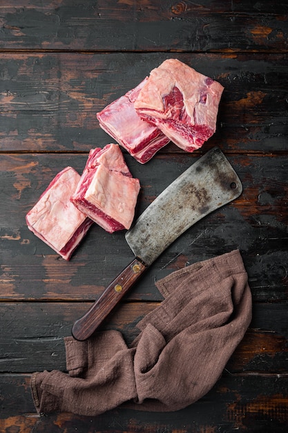 Conjunto de costillas de carne cruda y cuchillo de carnicero viejo, sobre fondo de mesa de madera oscura vieja, vista superior plana, con espacio para copiar texto