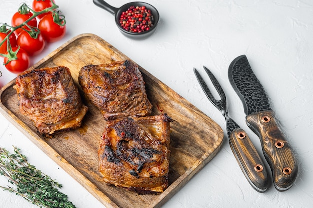 Conjunto de costillas de ternera a la parrilla, con ingredientes, sobre mesa de piedra blanca