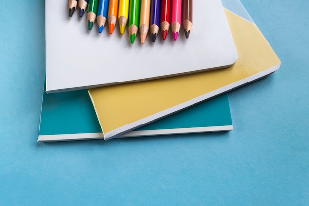 Conjunto de cuadernos y lápices de colores sobre un fondo verde con espacio para texto. Accesorios escolares. Lay Flat