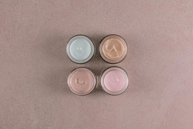 Un conjunto de cuatro frascos cosméticos de vidrio abiertos con diferentes tipos de cremas para el cuidado de la cara y el cuerpo de textura multicolor Vista superior