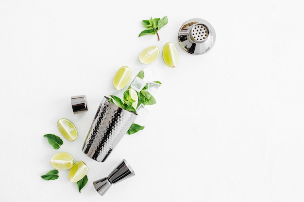Conjunto de acessórios de bar para fazer coquetéis. Shaker, jigger, copo, colher e outras ferramentas de barra com folhas de limão e hortelã no fundo withe.