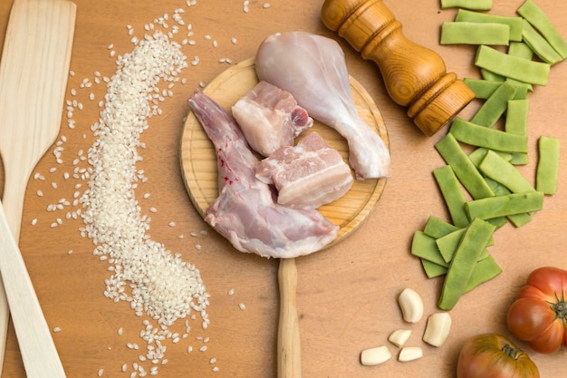 Conjunto de alimentos crus para preparar um arroz com frango e coelho Carne no centro arroz alho feijão verde tomate sal e pimenta e duas conchas