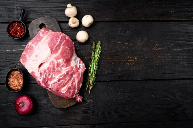 Conjunto de bife de carne de pescoço de porco, com ingredientes e ervas, no fundo preto da mesa de madeira, vista superior plana leiga, com espaço de cópia para o texto