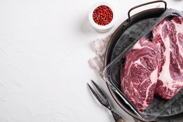 Conjunto de bifes de carne crua orgânicos embalados a vácuo Chuck Eye Roll, no fundo da mesa de pedra branca, vista superior plana, com espaço de cópia para texto