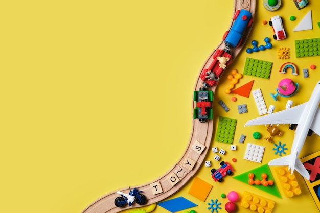 Foto conjunto de brinquedos infantis diferentes, ferrovia de madeira, trem, construtor em uma superfície amarela