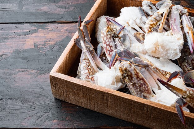 Conjunto de carne congelada de caranguejo nadador azul crua, em caixa de madeira, sobre mesa de madeira escura