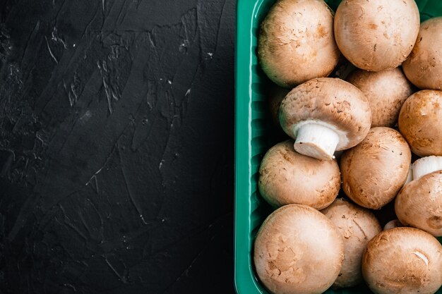 Conjunto de champignon de cogumelos crus, em fundo preto, em embalagem plástica, vista de cima plana lay, com espaço para texto copyspace