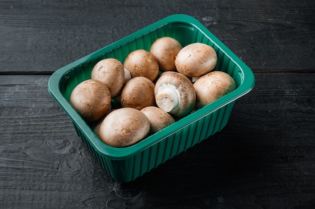 Conjunto de champignon de cogumelos crus, no fundo preto da mesa de madeira, em embalagem plástica